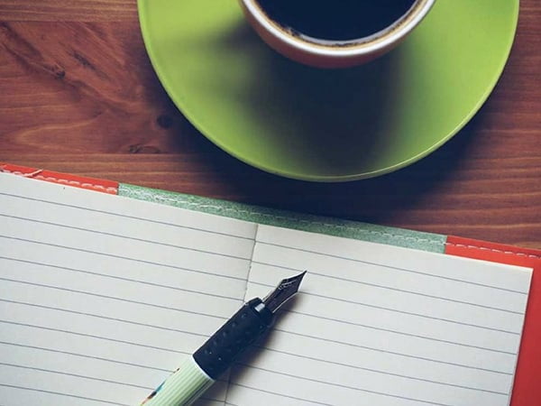 pen on notebook with coffee cup